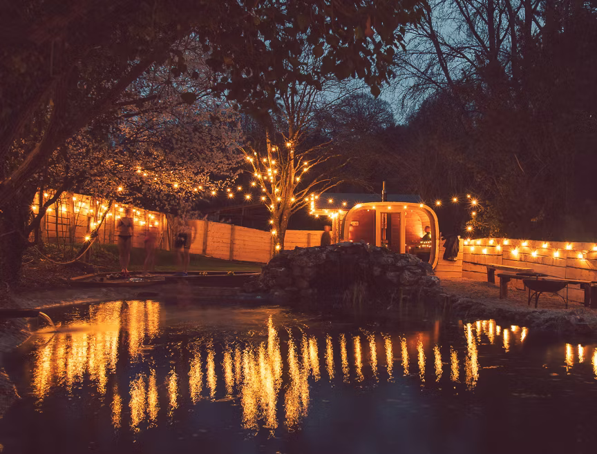 A night time scene of a beautiful spa location with warm fairy lights showing a sauna and an outdoor cold plunge pool full of water, in Westbury-on-Trym Bristol