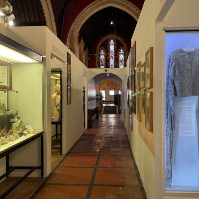 Museum interior shown at Glenside Hospital Museum, with medical collection of pharmacy items and medicines alongside a Victorian straitjacket in a display cabinet. Stained glass windows shown within a listed building, the former hospital chapel at Bristol Lunatic Asylum