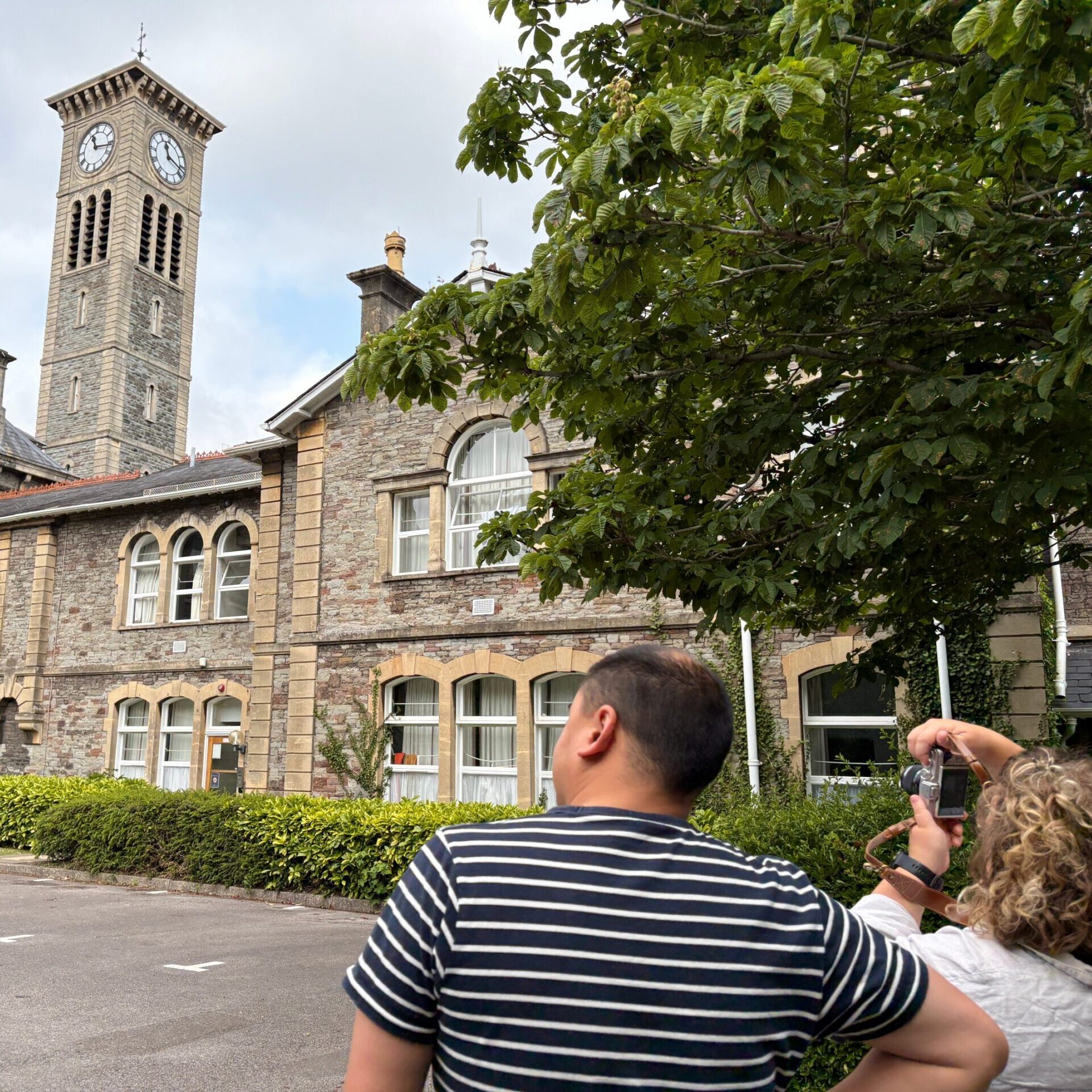 A couple on a free day out together in Bristol together, taking photos during a walking history group tour at former Glenside Hospital in Fishponds, looking at the clock tower. Listed building